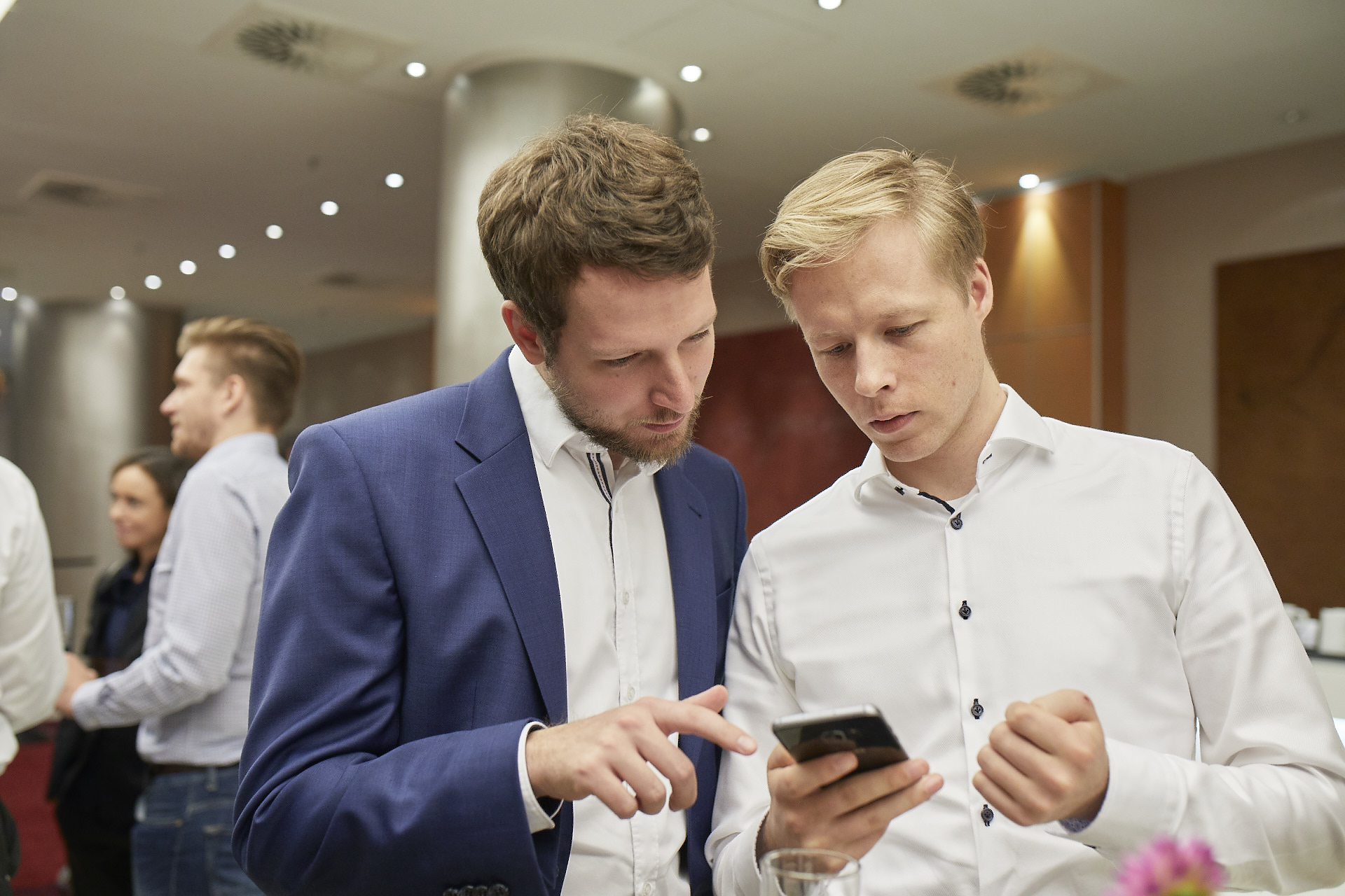 Geschäftsmann zeigt seinem Partner etwas auf seinem Handy an einer Konferenz