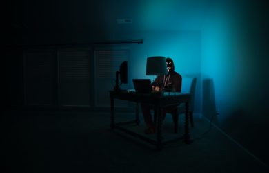 Anonyme Person sitzt im dunklen Raum auf seinem Laptop