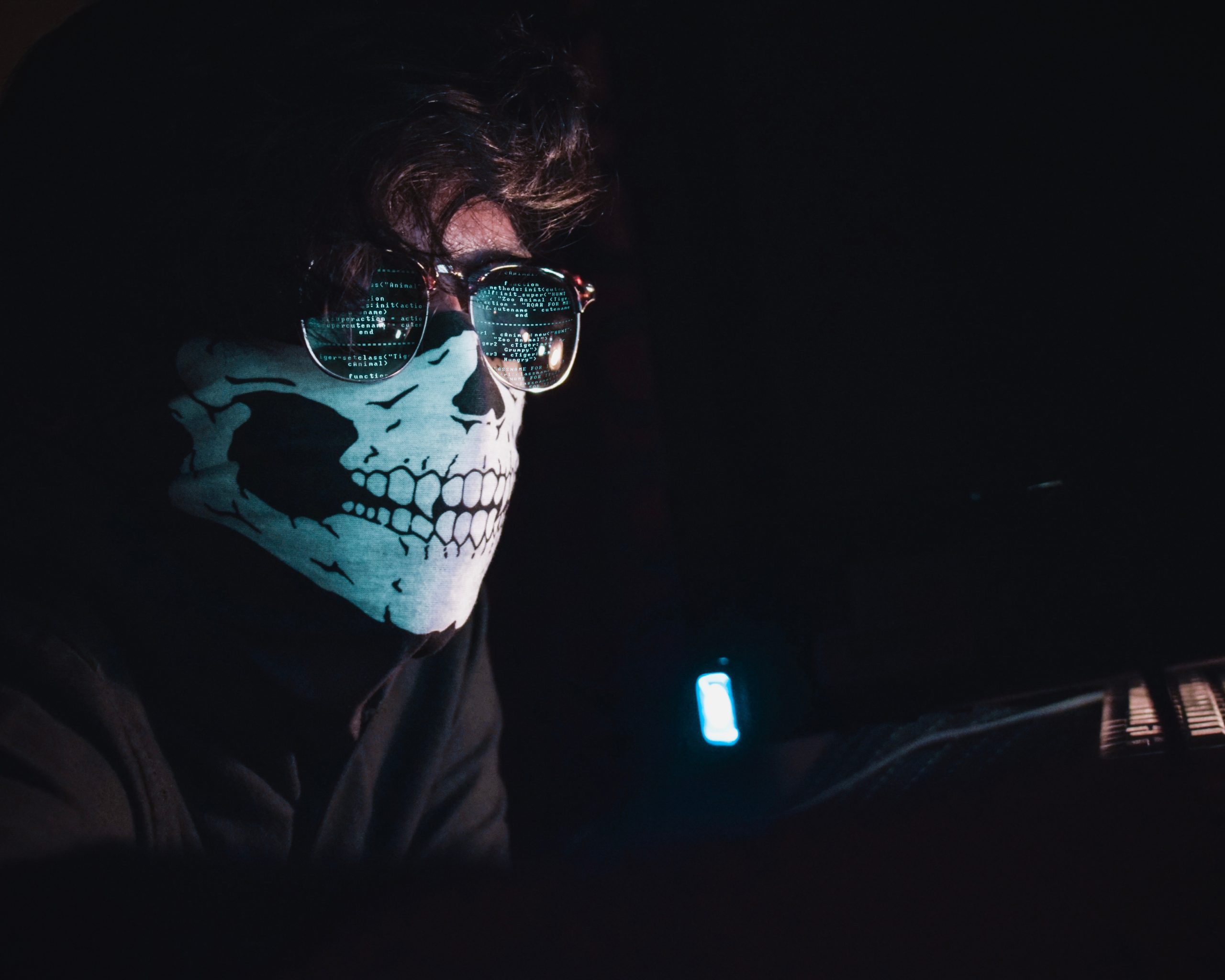 Mann mit einer Maske und Sonnebrille sitzt im dunklen Raum und kodiert
