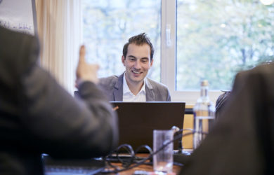 Mann sitzt bei einer Konferenz hinter seinem Laptop