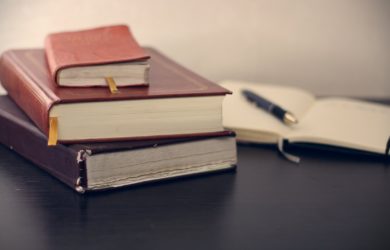 regulatorische anforderungen banken: Bücher aufeinander gestapelt mit offenem notizbuch im Hintergrund