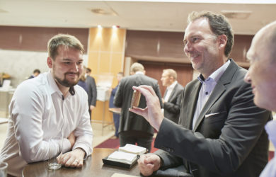 Geschäftsmann zeigt anderen Männern etwas auf seinem Handy auf einer Konferenz