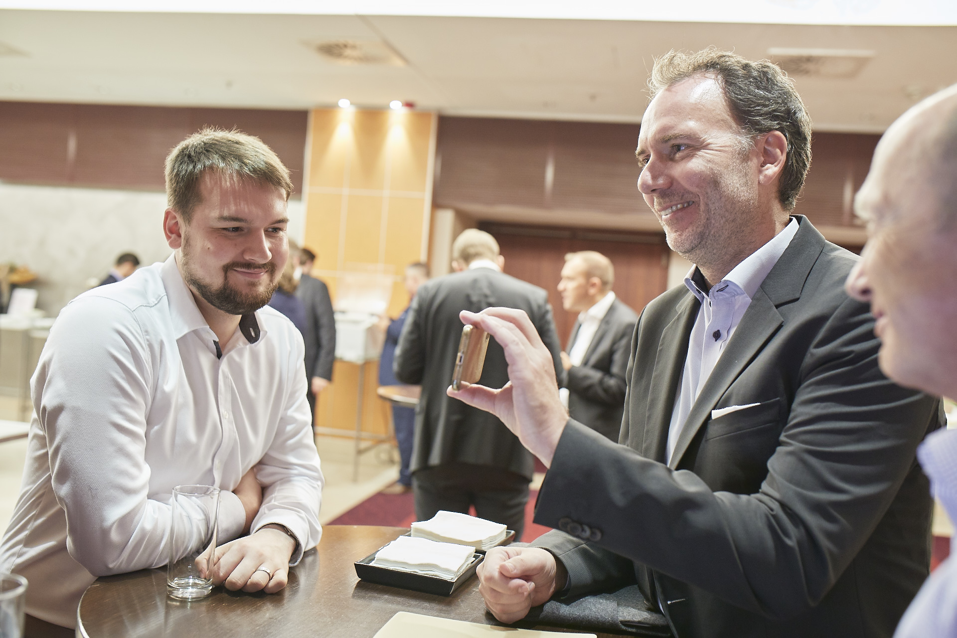 Geschäftsmann zeigt anderen Männern etwas auf seinem Handy auf einer Konferenz