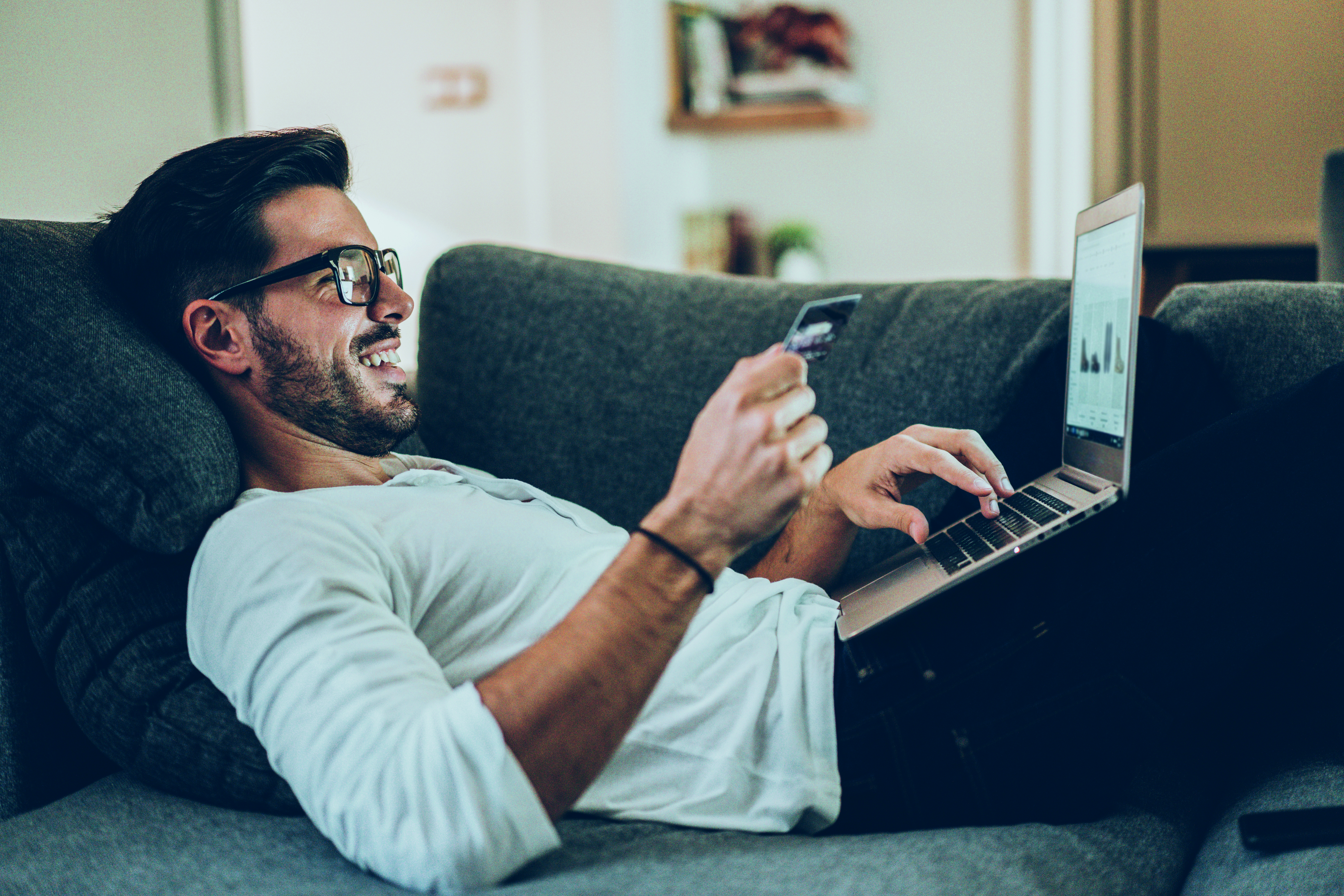 Mann sitzt auf dem Sofa und bestellt Sachen online auf dem laptop