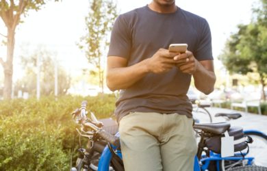 Mann mit Smartphone in der Hand lehnt sich an seinem Fahrrad im Park