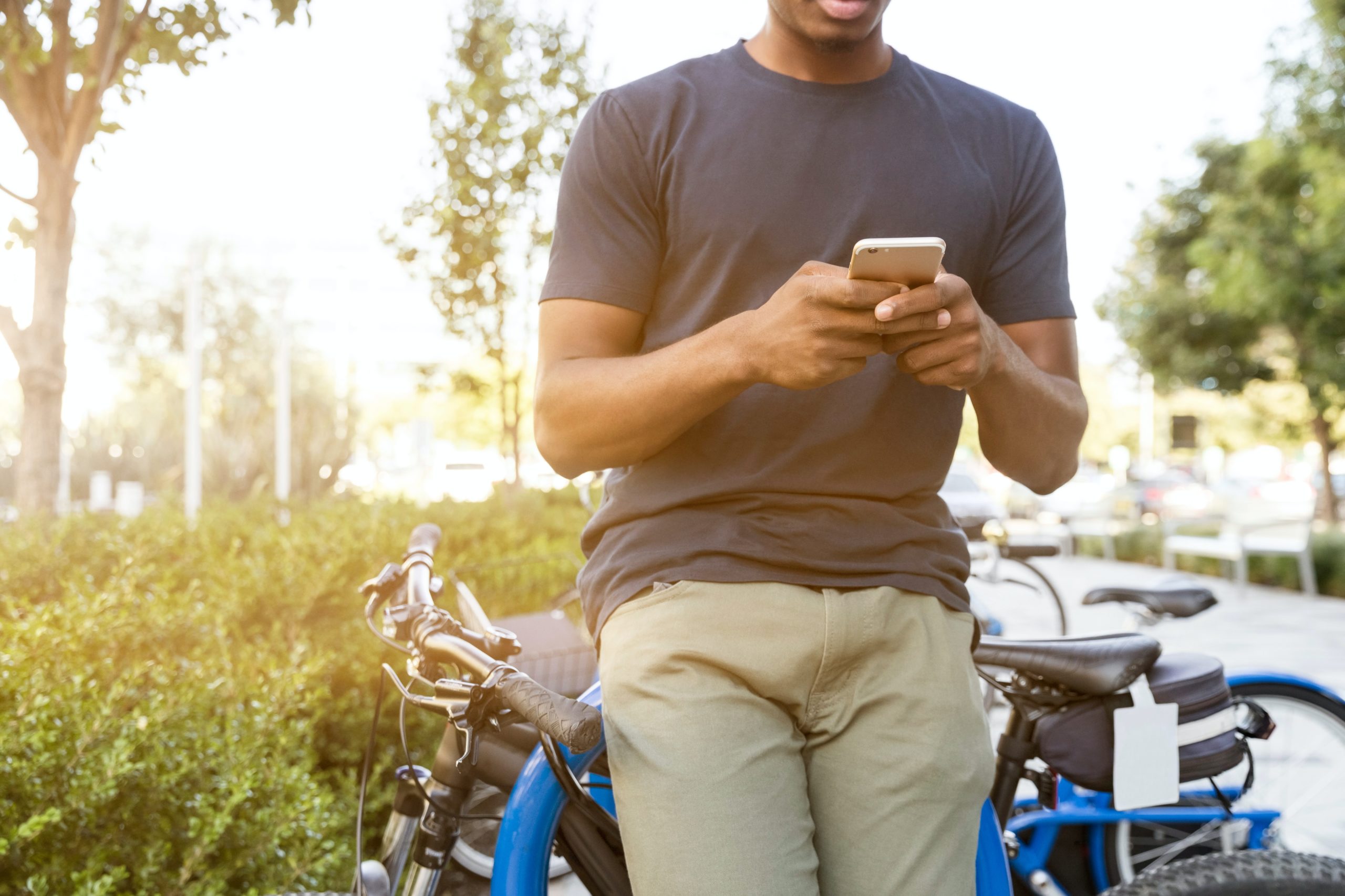 Mann mit Smartphone in der Hand lehnt sich an seinem Fahrrad im Park