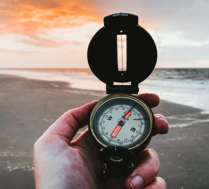 Agile transformation: Mann hält Kompass mit Strand im Hintergrund