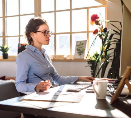 Arbeiterin arbeitet im Home-Office, sitz vor ihrem Computer und schreibt Notizen auf