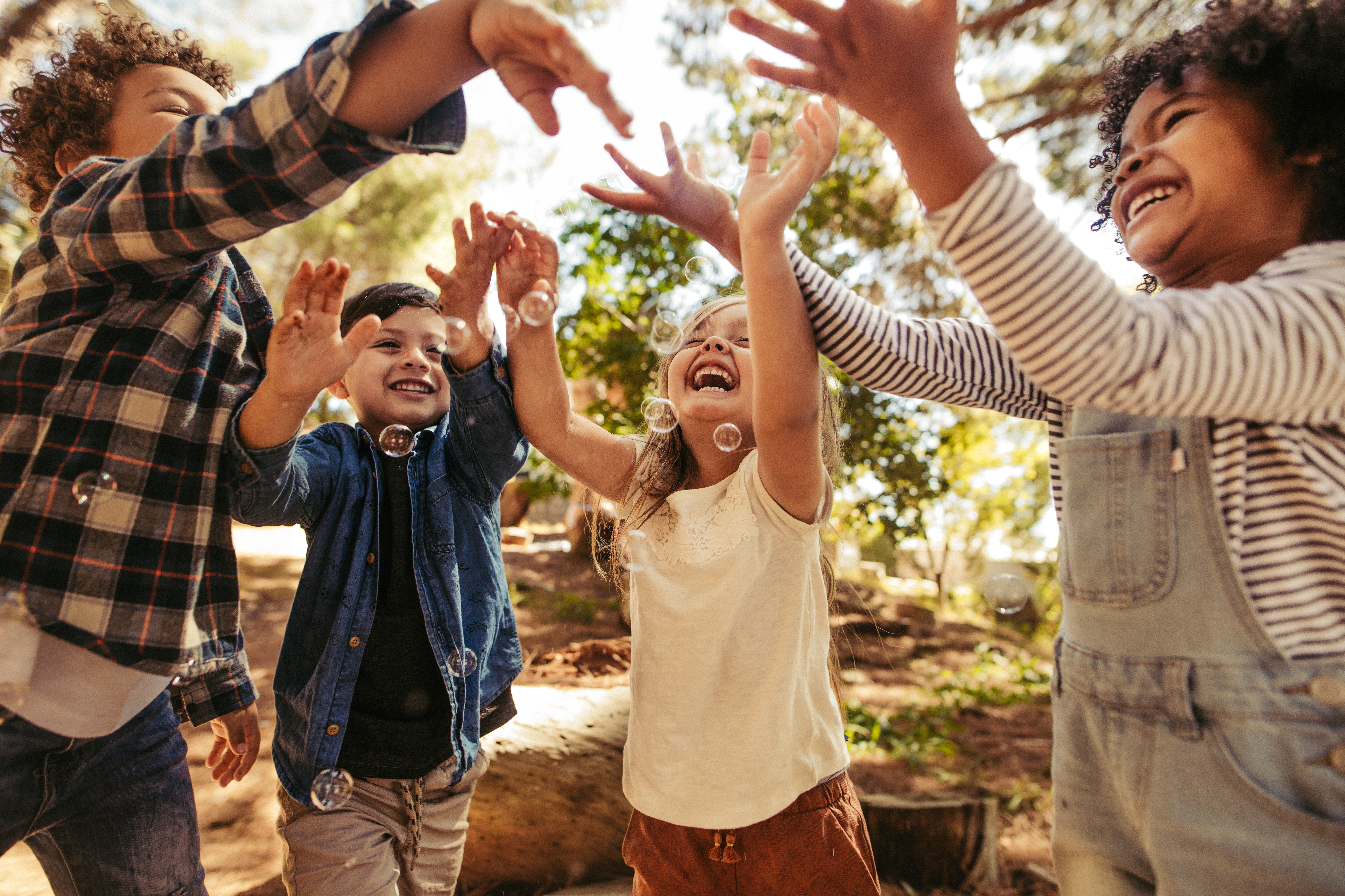 Kindergruppe spielt mit Seifenblasen im Wald. Junge bläst Seifenblasen mit Freunden, die versuchen, die Blasen zu fangen.