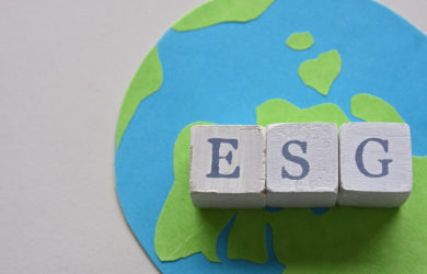 auf einem weißen Hintergrund ist aus Papier geschnittene Abbildung von der Erde, worauf Holzwürfel liegen die das Wort ESG zusammen bilden