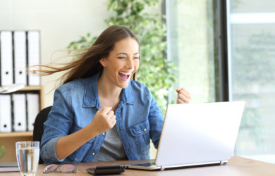 Aufgeregte Frau sitzt vor ihrem Laptop und freut sich über einen Erfolg