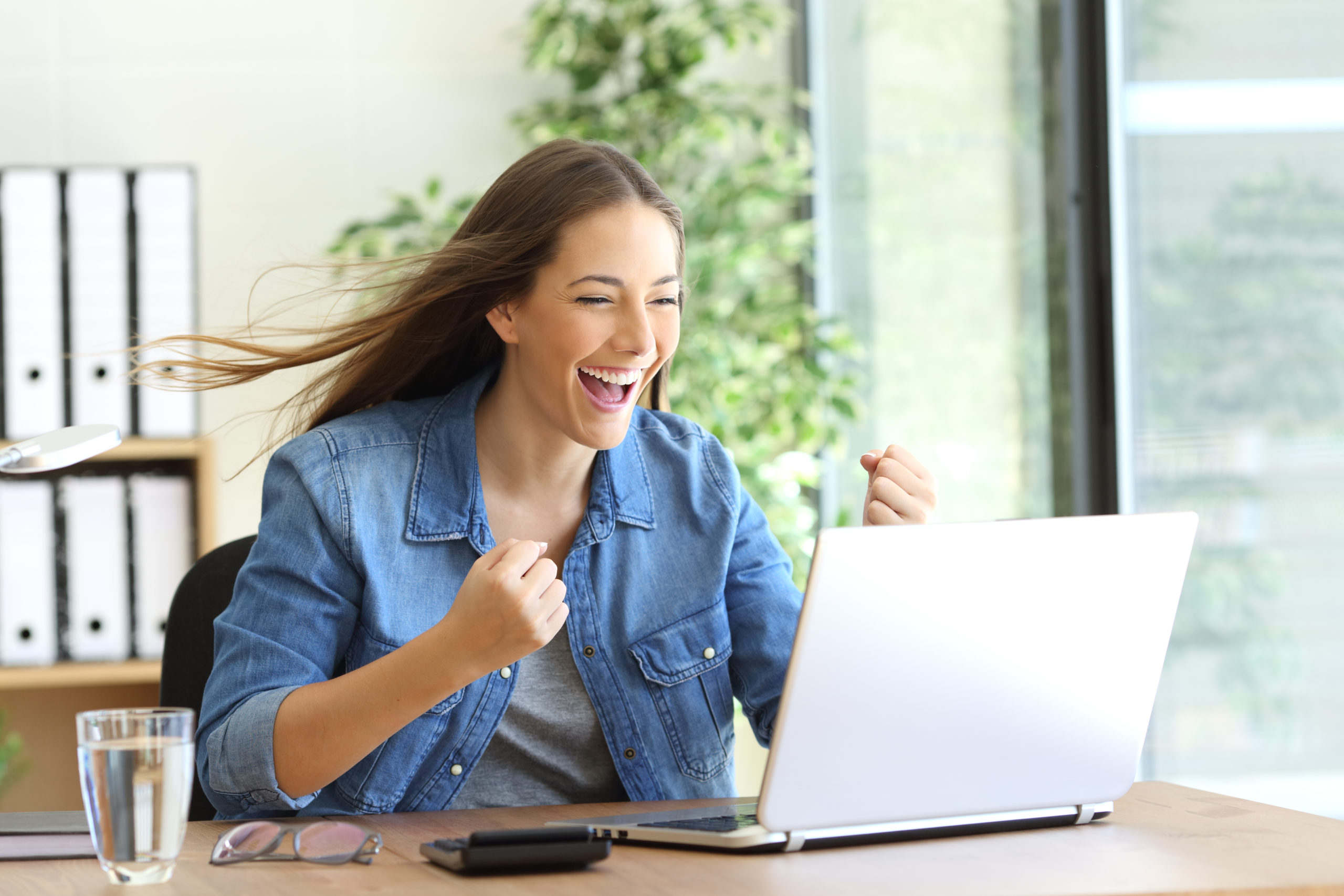 Aufgeregte Frau sitzt vor ihrem Laptop und freut sich über einen Erfolg