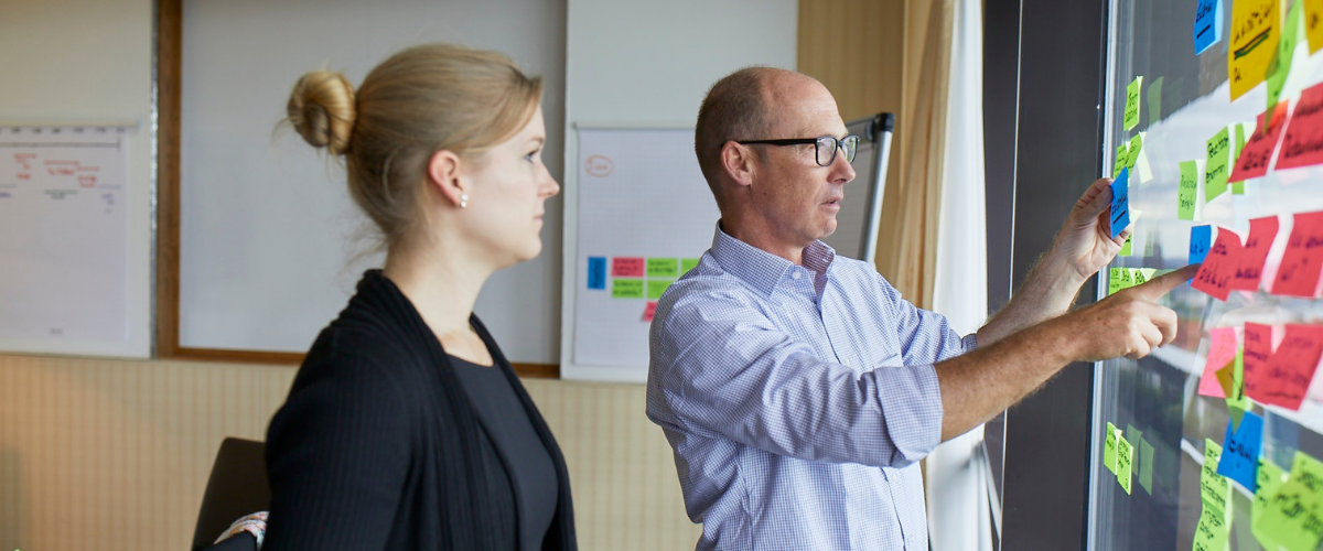 Zwei Kollegen brainstormen Idden auf einer Tafel mit der Hilfe von farbigen Post-It Notes