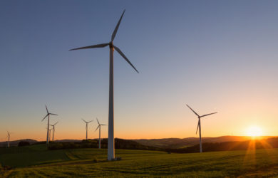 Windkraftanlagen bei Sonnenuntergang auf einem grünem Feld