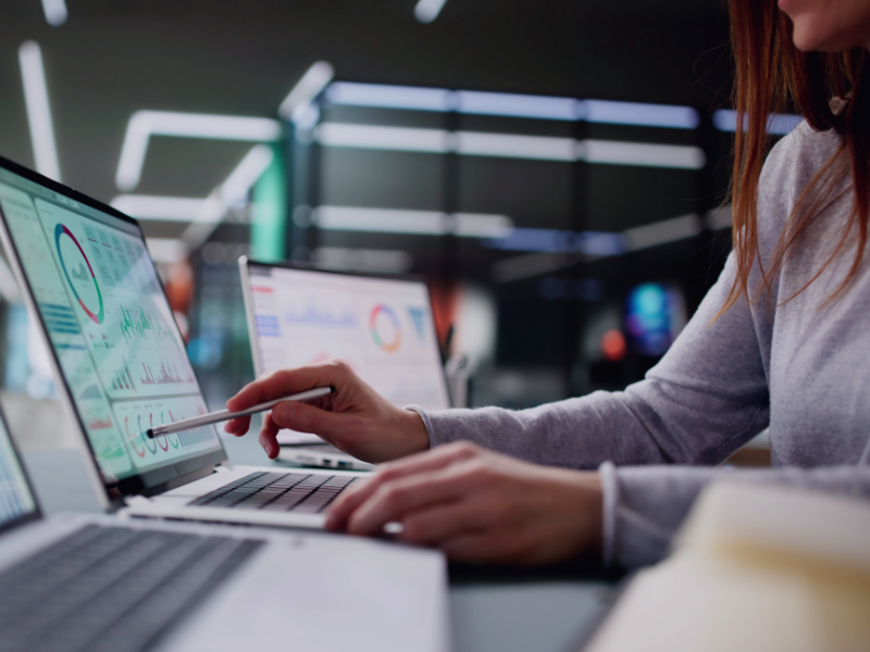 Frau analysiert Dashboards mit Diagrammen und KPIs auf mehreren Laptops – Symbolbild für datengetriebene IT-Beratung und Data Mesh