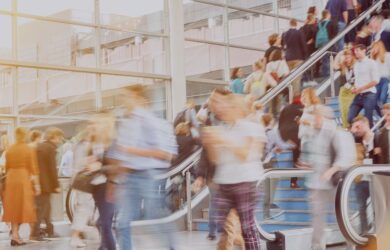 Viele Menschen bewegen sich in einer modernen Halle mit Rolltreppen, teilweise unscharf durch Bewegung, symbolisch für Vernetzung auf der IFAT München
