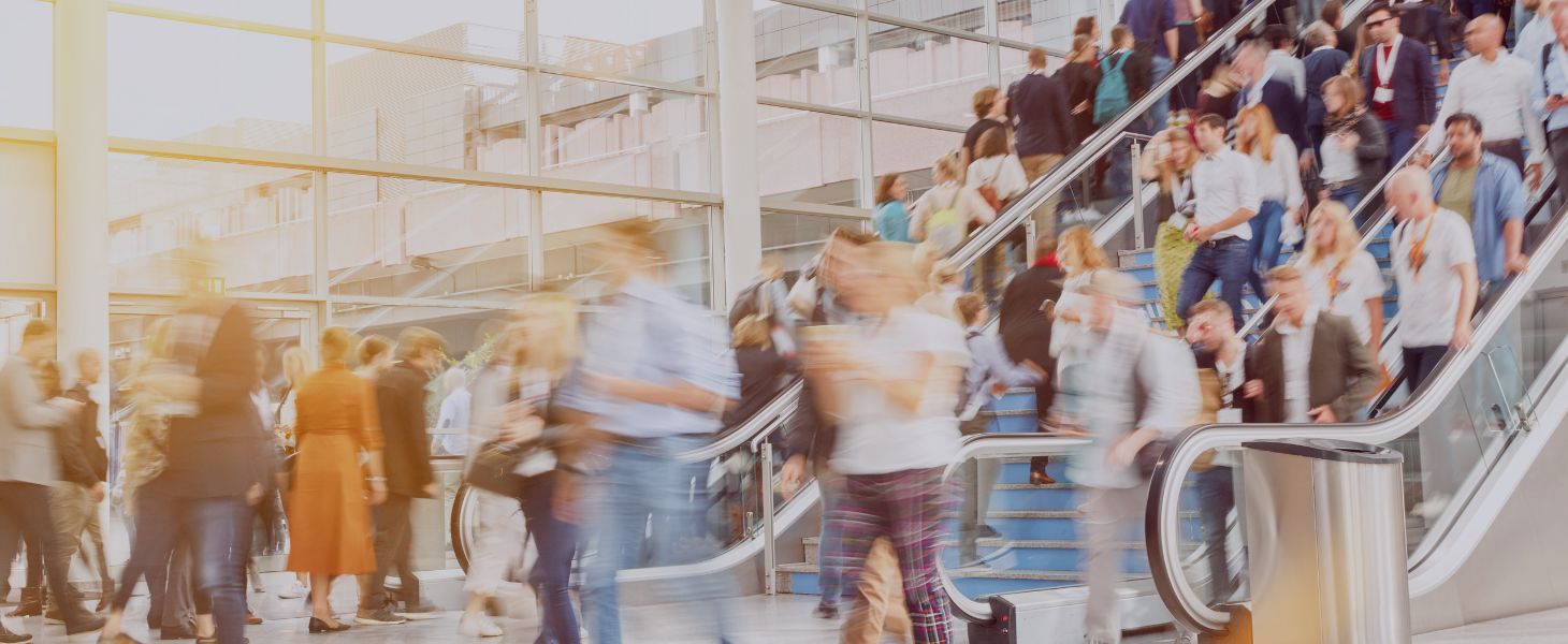 Viele Menschen bewegen sich in einer modernen Halle mit Rolltreppen, teilweise unscharf durch Bewegung, symbolisch für Vernetzung auf der IFAT München