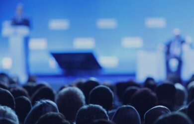 Publikum bei einer Konferenz mit Bühne und Vortrag, symbolisch für Austausch, Networking und Wissenstransfer