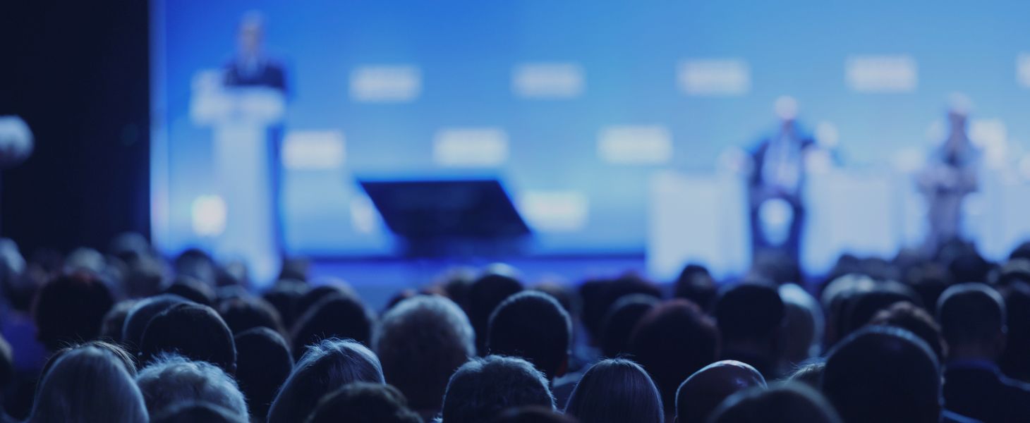 Publikum bei einer Konferenz mit Bühne und Vortrag, symbolisch für Austausch, Networking und Wissenstransfer