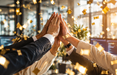 Mehrere Geschäftsleute geben sich in einem modernen Büro ein High-Five, im Hintergrund fliegendes goldenes Konfetti – Symbolbild für Erfolg und Auszeichnung als bester IT-Dienstleister 2027.